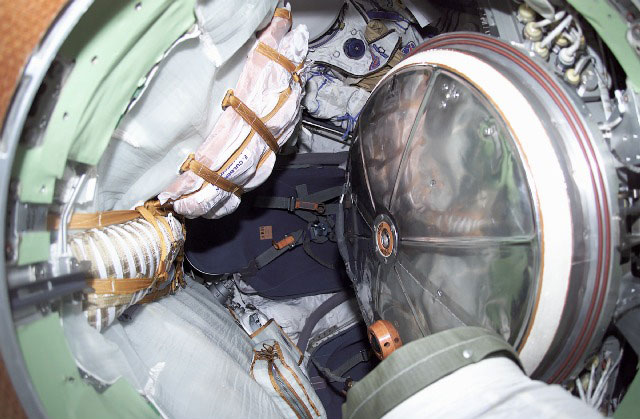 Interior view of Soyuz spacecraft with Sokol suits, hatch, and crew seats.