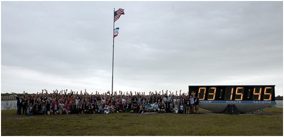 A large group of people stand next to a large clock